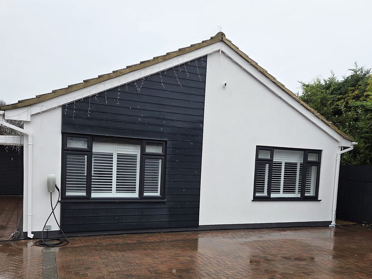 Bungalow with freshly rendered white walls beside dark cladding on the front