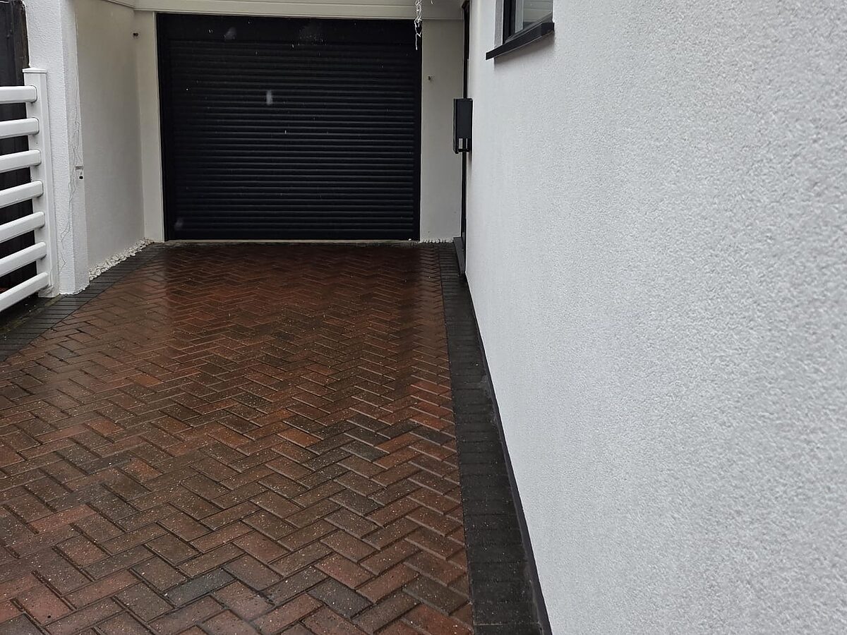 Freshly rendered side wall of a bungalow, showing its even textured finish along a block-paved drive