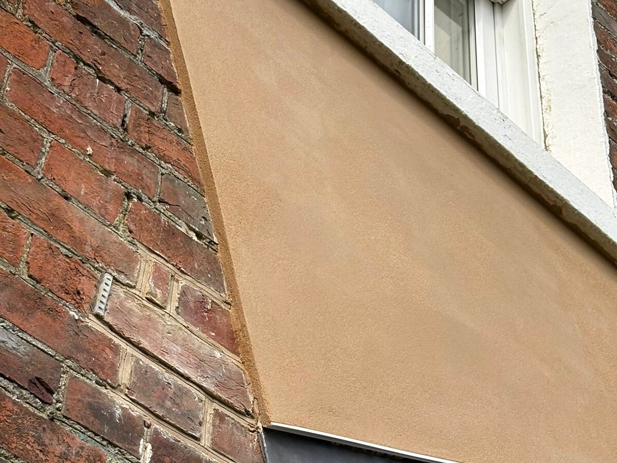 Freshly rendered panel above a bay window on a red-brick period house